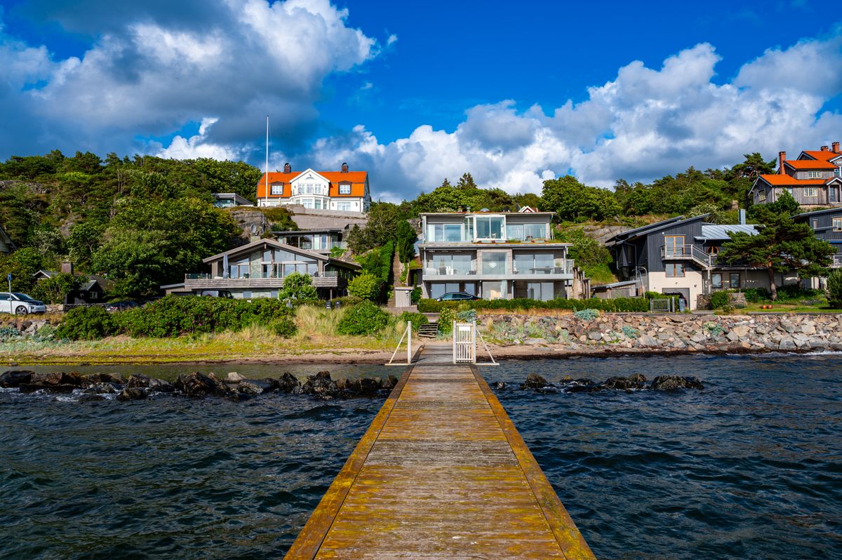 Kustnära hus med stora glaspartier och en brygga i förgrunden.