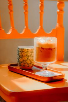 Stylish coffee and tea setup on a vibrant orange table with warm lighting.