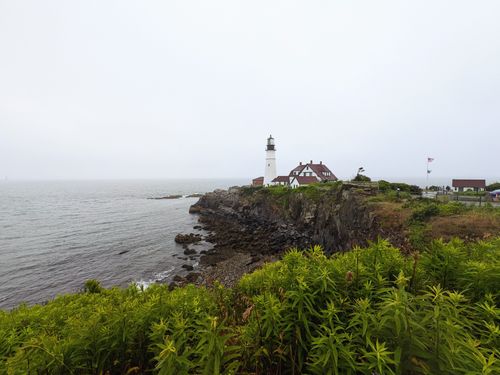 Free Scenic view of the iconic Portland Head Light perched on rocky cliffs, surrounded by lush greenery. Stock Photo