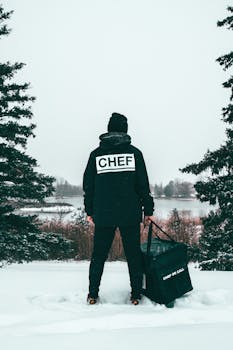 冬天，厨师拿着送货袋，站在湖边雪地里，四周是结冰的湖面和常绿树林