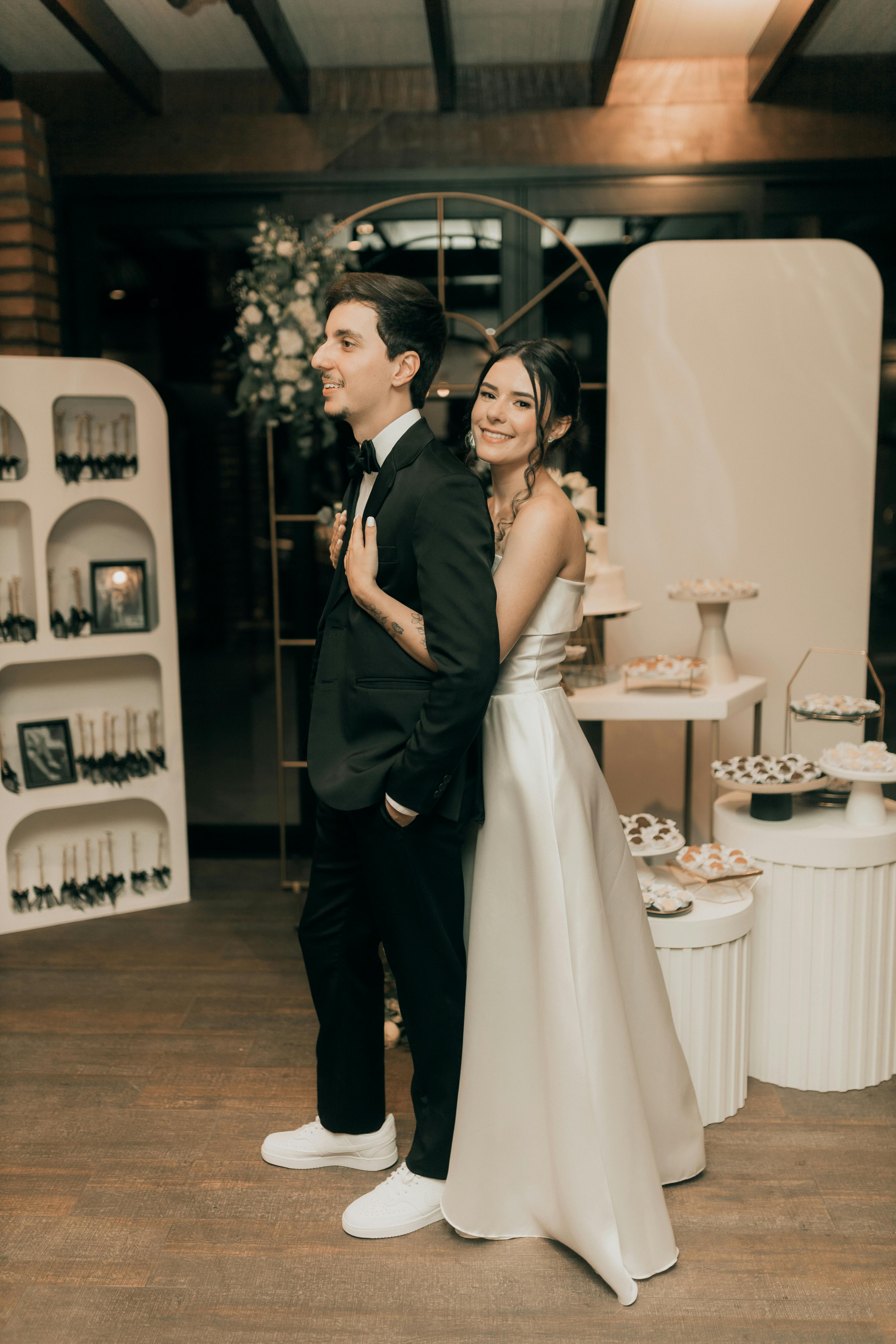 A happy bride and groom posing back-to-back in an elegant indoor wedding reception setting.