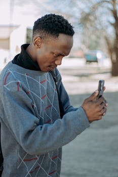 Casual young man interacting with smartphone outdoors in bright sunlight.