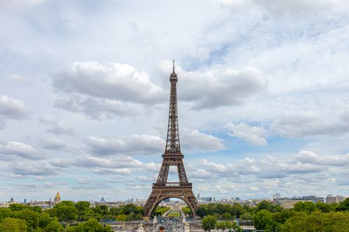 Free A stunning view of the Eiffel Tower in Paris surrounded by lush greenery under a cloudy blue sky. Stock Photo