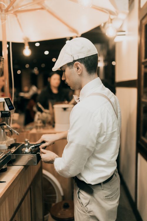 Free Barista in a cozy cafe preparing coffee at night under warm lighting. Stock Photo