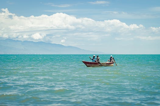 Three individuals in a wooden boat paddling through clear turquoise ocean under a bright sky.