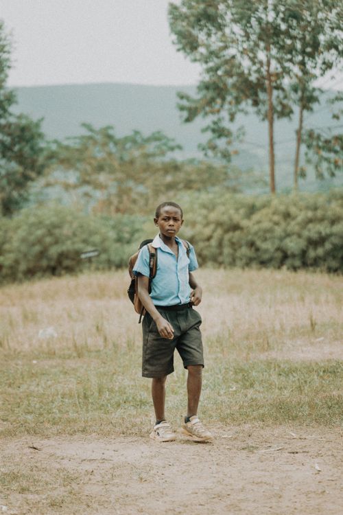 Free A young boy in school uniform stands outdoors with a backpack, facing the camera. Stock Photo