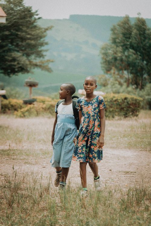 Free Two young girls in dresses walking outdoors in a lush Ugandan landscape, capturing a serene moment of friendship. Stock Photo