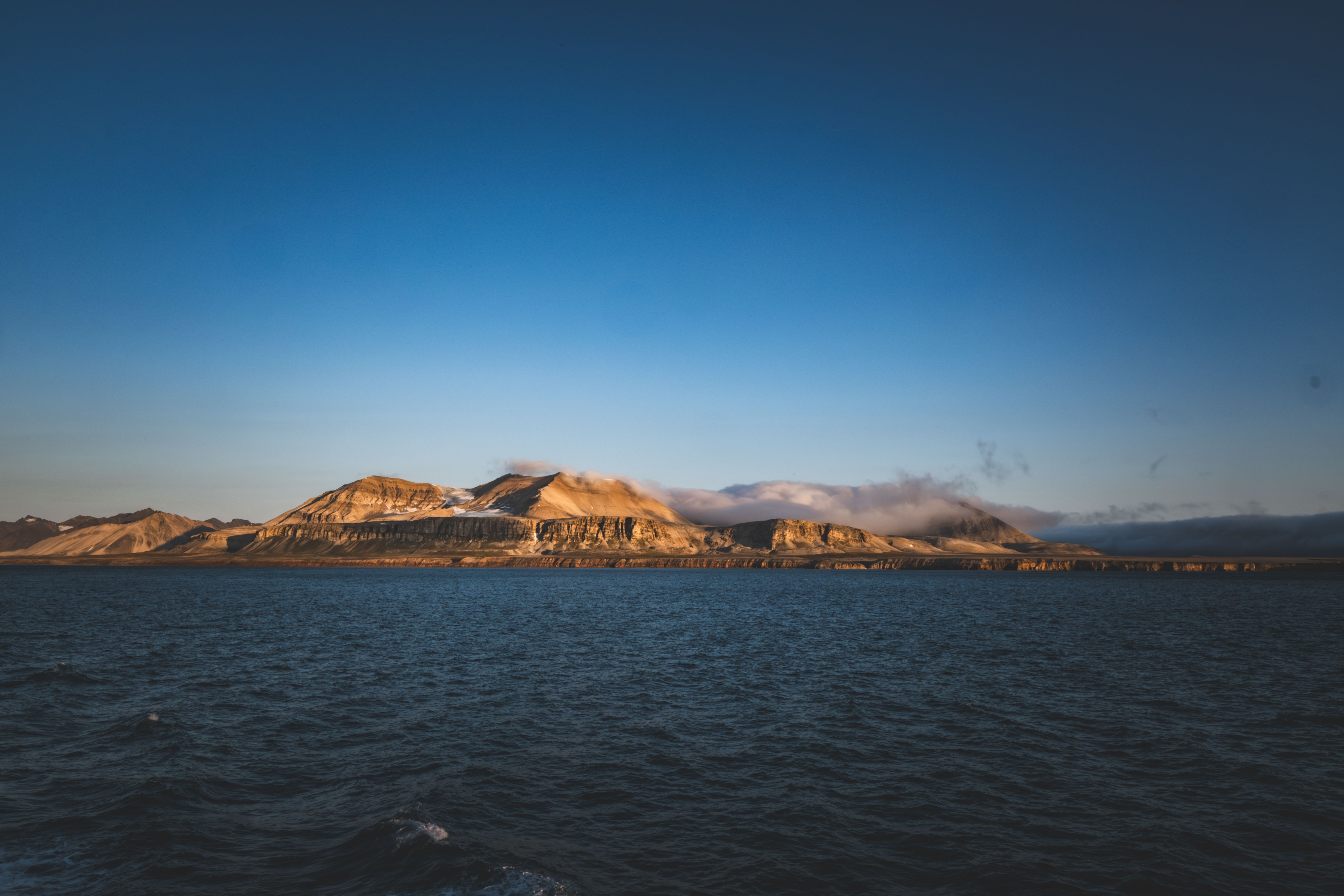 Breathtaking view of Arctic mountains and ocean under clear twilight sky, capturing serene beauty.