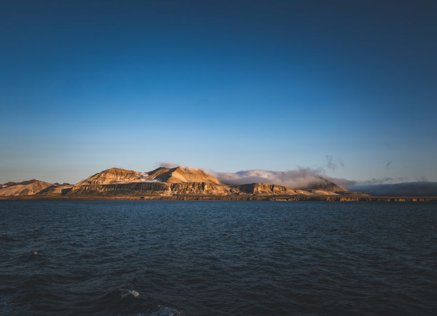 Breathtaking view of Arctic mountains and ocean under clear twilight sky, capturing serene beauty.