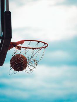 A basketball sinking through a hoop outdoors with a clear blue sky as the backdrop.