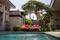 一名年轻人跳进巴厘岛热带度假村的泳池，捕捉到了夏日休闲与旅行的精髓