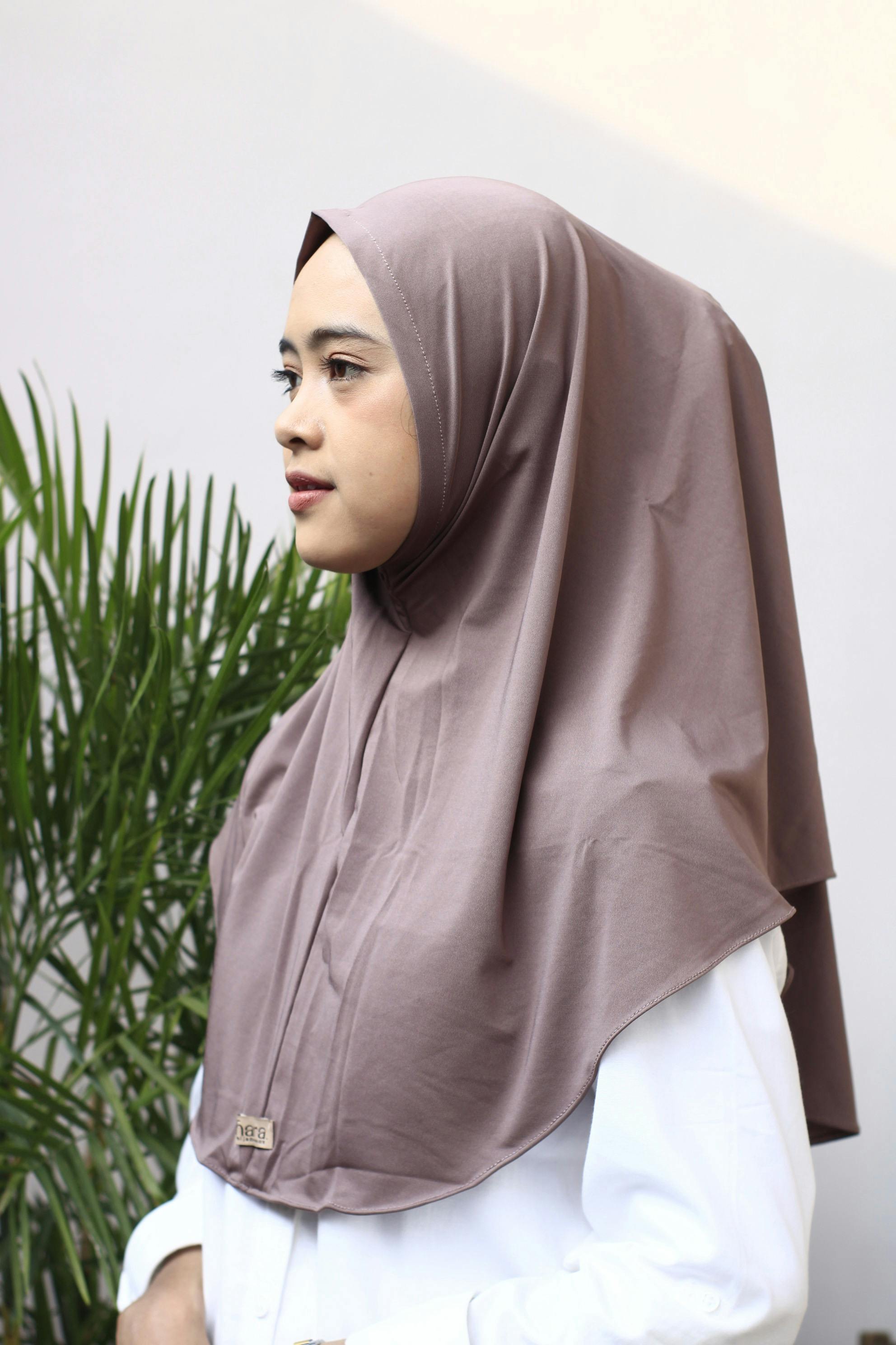 Side profile of a woman wearing a hijab, outdoors, with plants.