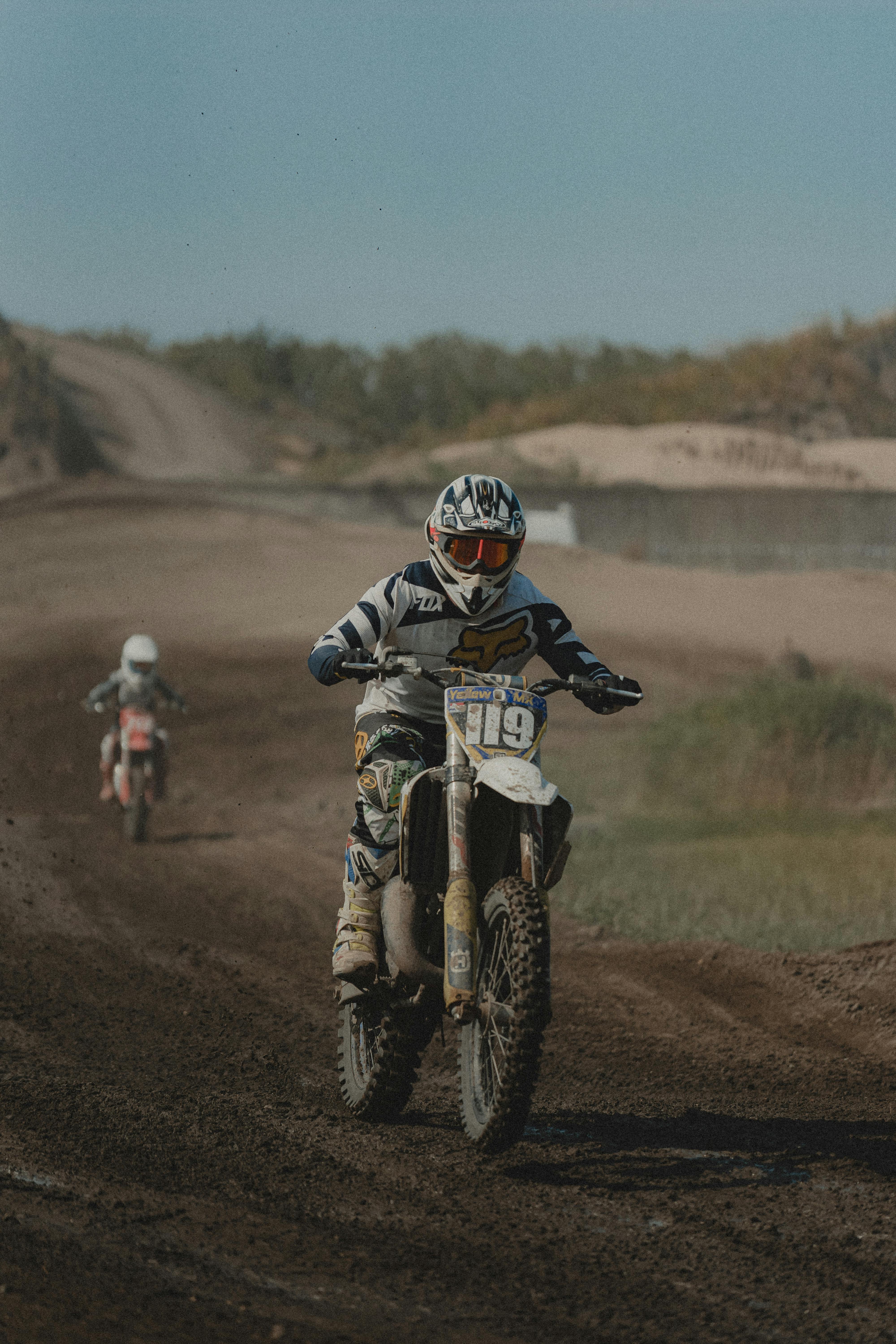 Riders maneuver through a challenging dirt track during a competitive motocross race under a clear sky.