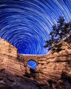Breathtaking star trail over a natural rock archway at night, showcasing the beauty of astronomy and landscapes.