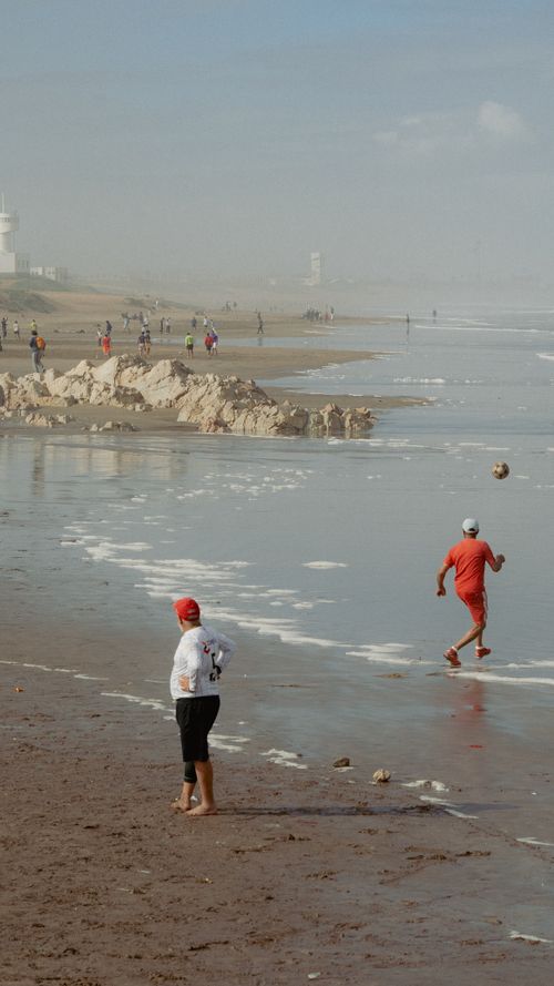 Free Casual soccer match on a foggy beach with people playing and walking along the shore. Stock Photo