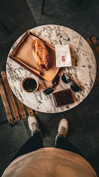 Overhead view of coffee and pastry with stylish accessories on a marble table, depicting a trendy urban lifestyle.