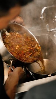 A chef pours steaming seafood broth into a pot, highlighting culinary skill.
