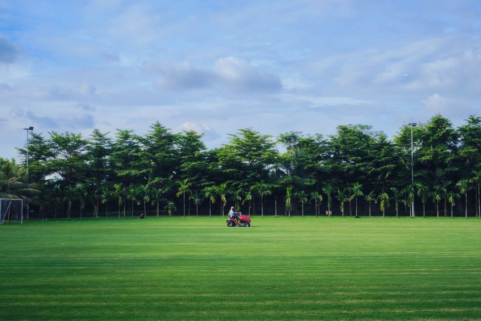 A man mowing the grass on a pristine golf course in Dhaka, Bangladesh, under a clear summer sky.
