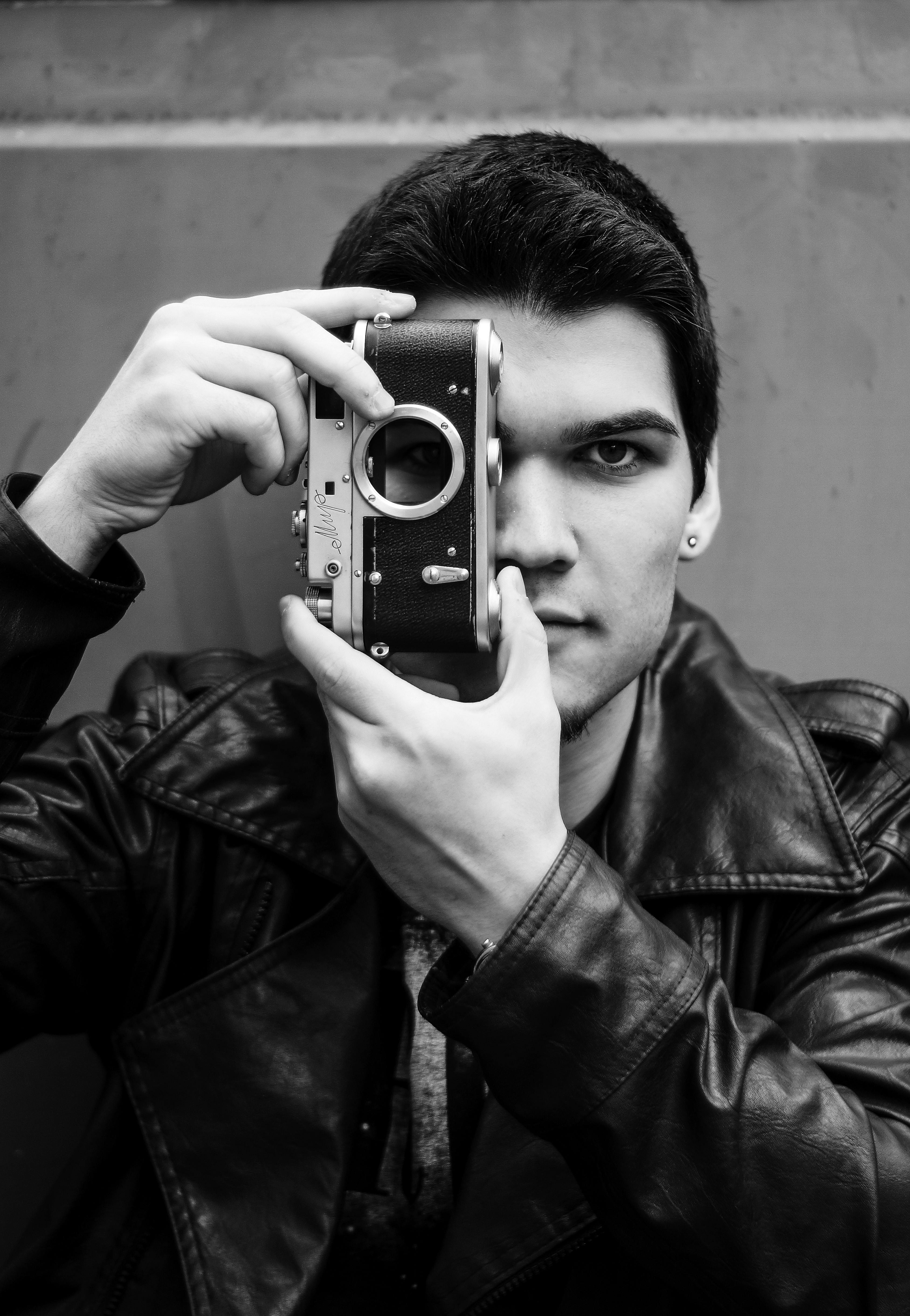 Artistic black and white portrait of a young man holding a vintage camera, capturing a classic and timeless feel.