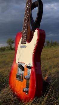 A vibrant red electric guitar stands in a grassy field at sunset, showcasing its sleek design and glossy finish.
