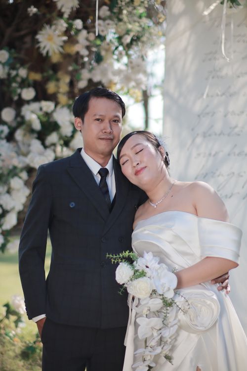 Free A happy couple poses at their wedding with a beautiful floral backdrop. Stock Photo