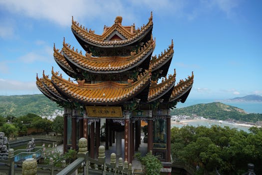 A picturesque Chinese temple overlooking lush hills and a serene coastline.