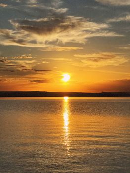 Serene sunset casting golden hues over calm lake surface with scattered clouds.