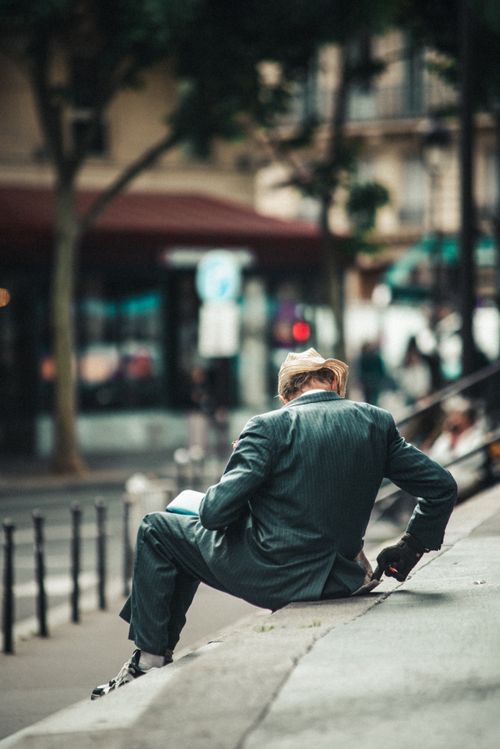 Free A man in a suit and hat sitting on a curb in a Paris street setting. Stock Photo
