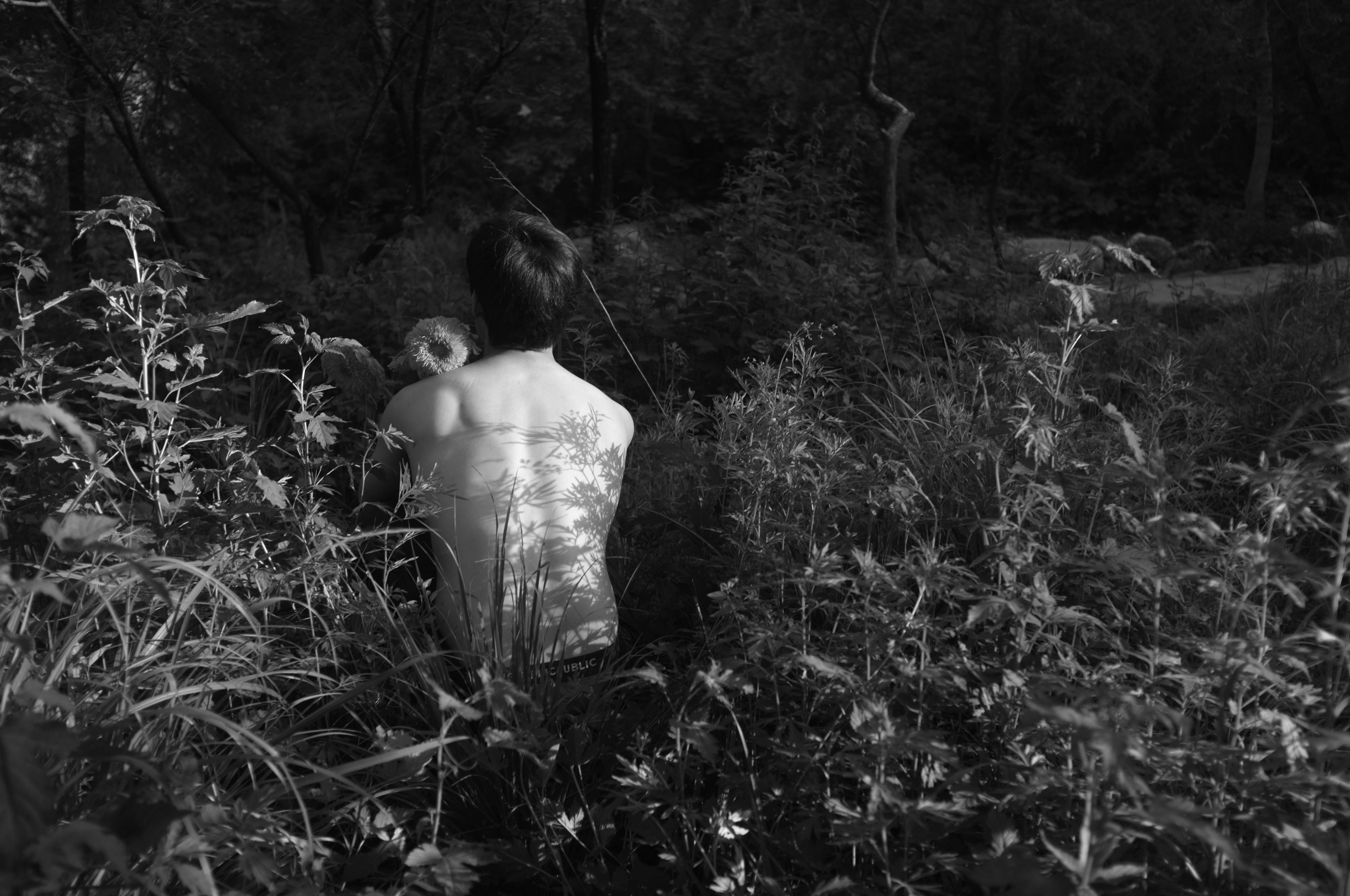 grayscale photo of topless man near plants