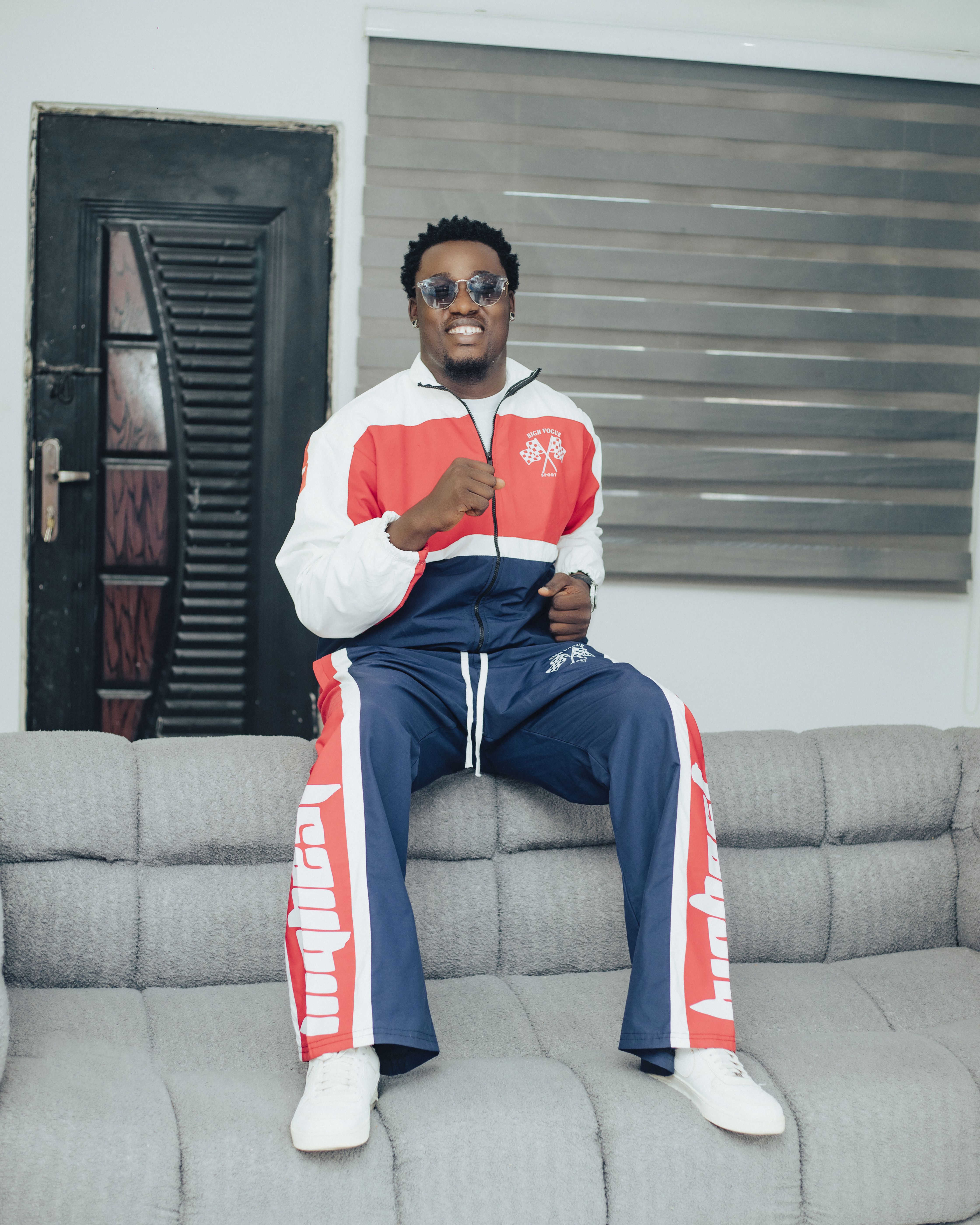 A stylish man smiling indoors, wearing a vibrant red and blue tracksuit, posing confidently.