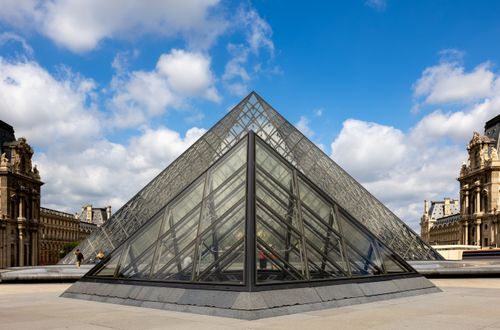 Free Iconic Louvre glass pyramid against a cloudy sky in Paris, France. Stock Photo
