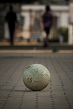 A soccer ball on a cobblestone path with silhouettes in the background, captured outdoors.