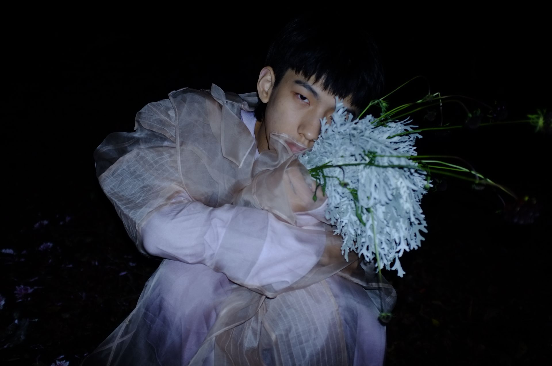 A creative nighttime portrait of a fashionable person holding a unique flower arrangement.