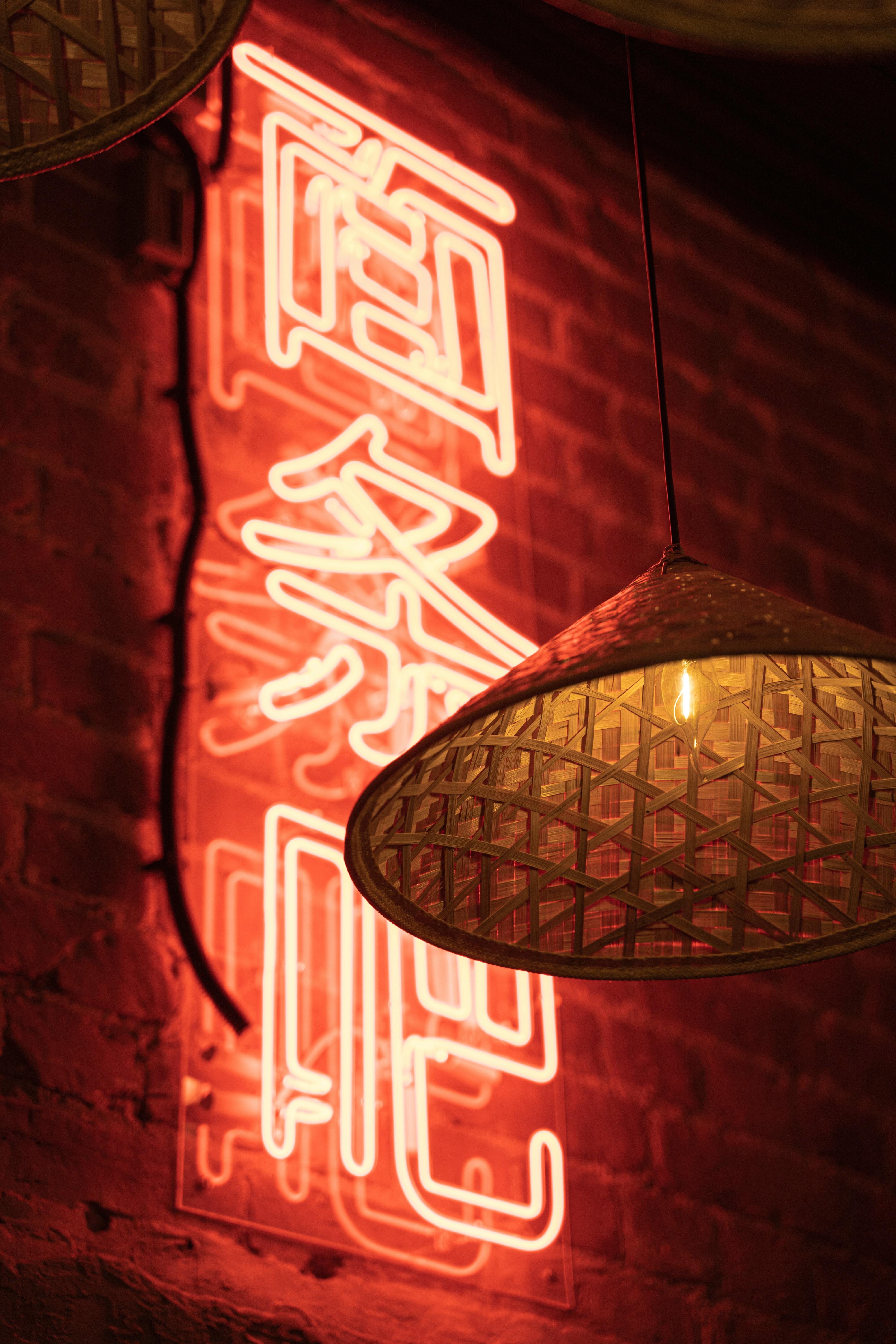 Warm ambiance with a glowing neon sign and wicker pendant lights in an urban interior.