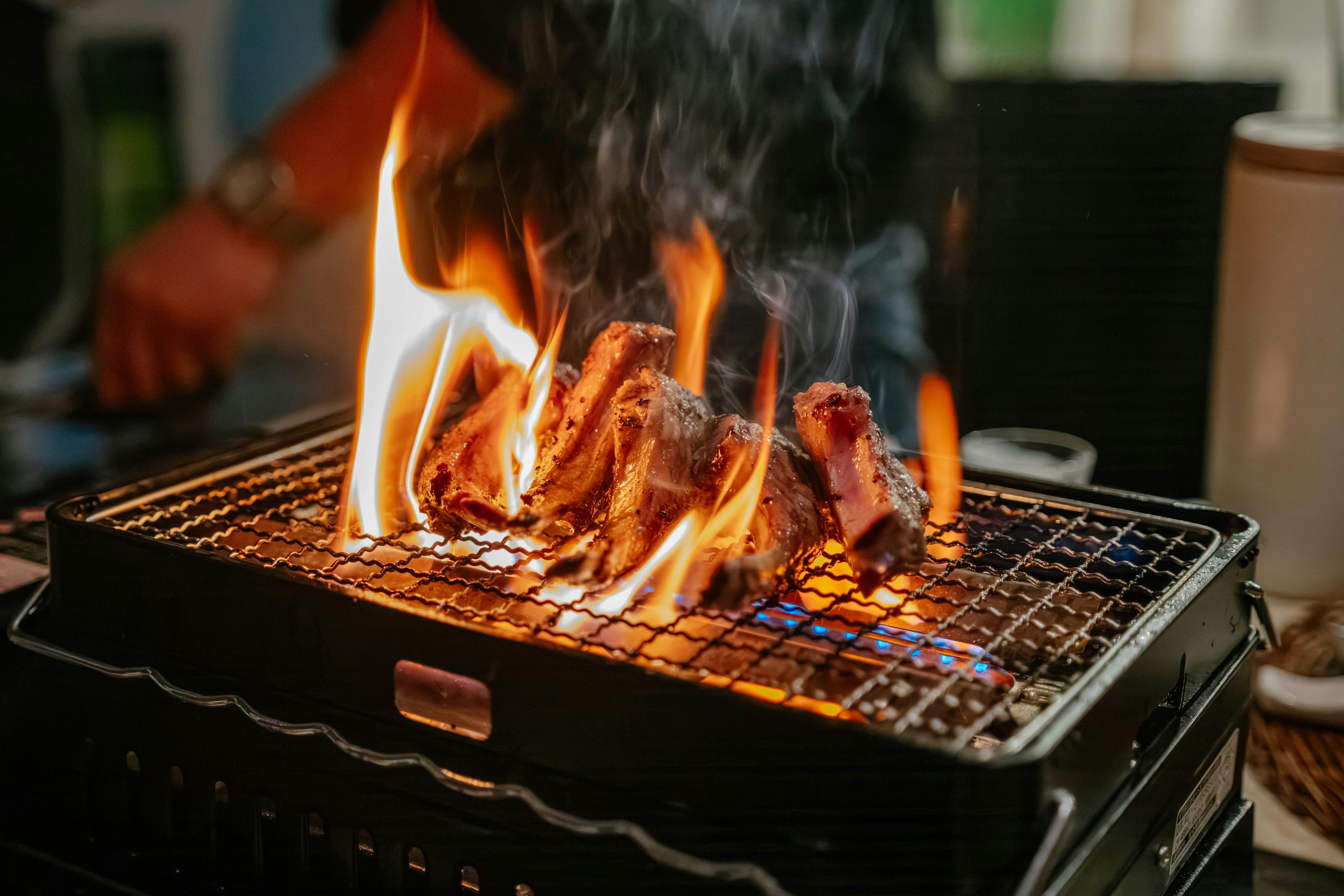 Delicious grilled meat being cooked on a flaming barbecue grill with visible smoke and flames.