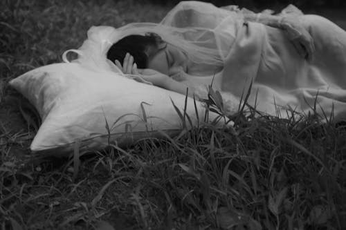 잔디 필드에 누워있는 여자의 회색조 사진