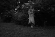 一幅黑白肖像空灵静谧，描绘了一位身着婚纱的女子，她正站在郁郁葱葱的绿地上