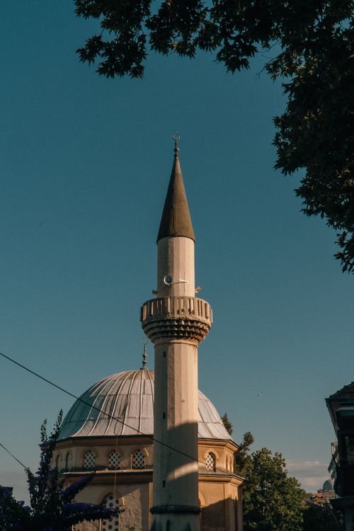 Free A beautifully lit minaret of a historic mosque surrounded by trees under a clear blue sky. Stock Photo