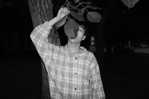 一幅黑白肖像描绘了一个人用树叶遮挡面部，站在户外的姿势