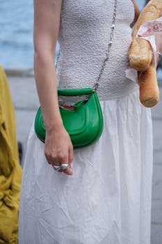 Elegant outfit featuring a green handbag and baguettes by the water.