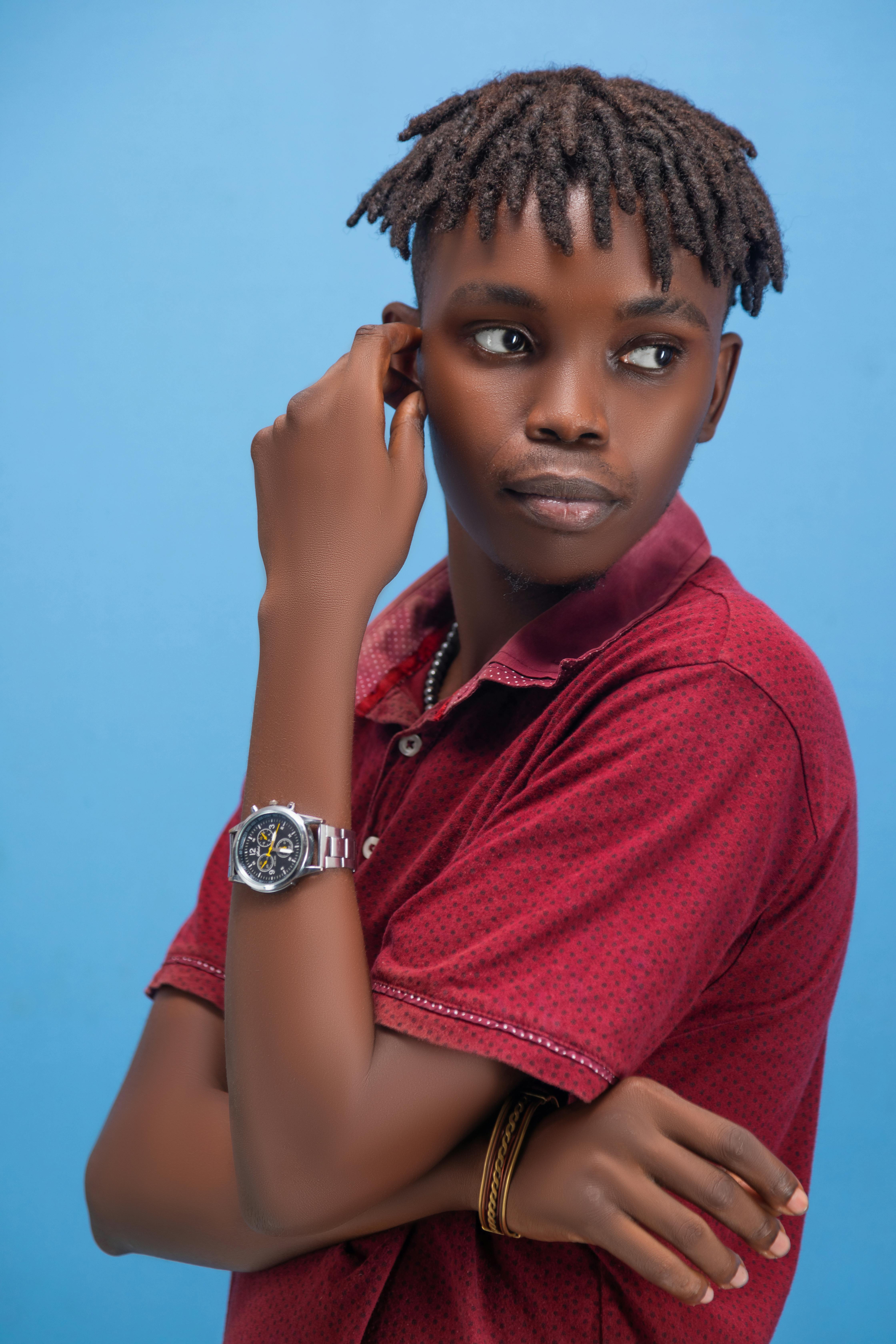 Gratuit Un jeune homme à la mode portant une montre et un bracelet pose avec assurance sur un fond bleu. Photos