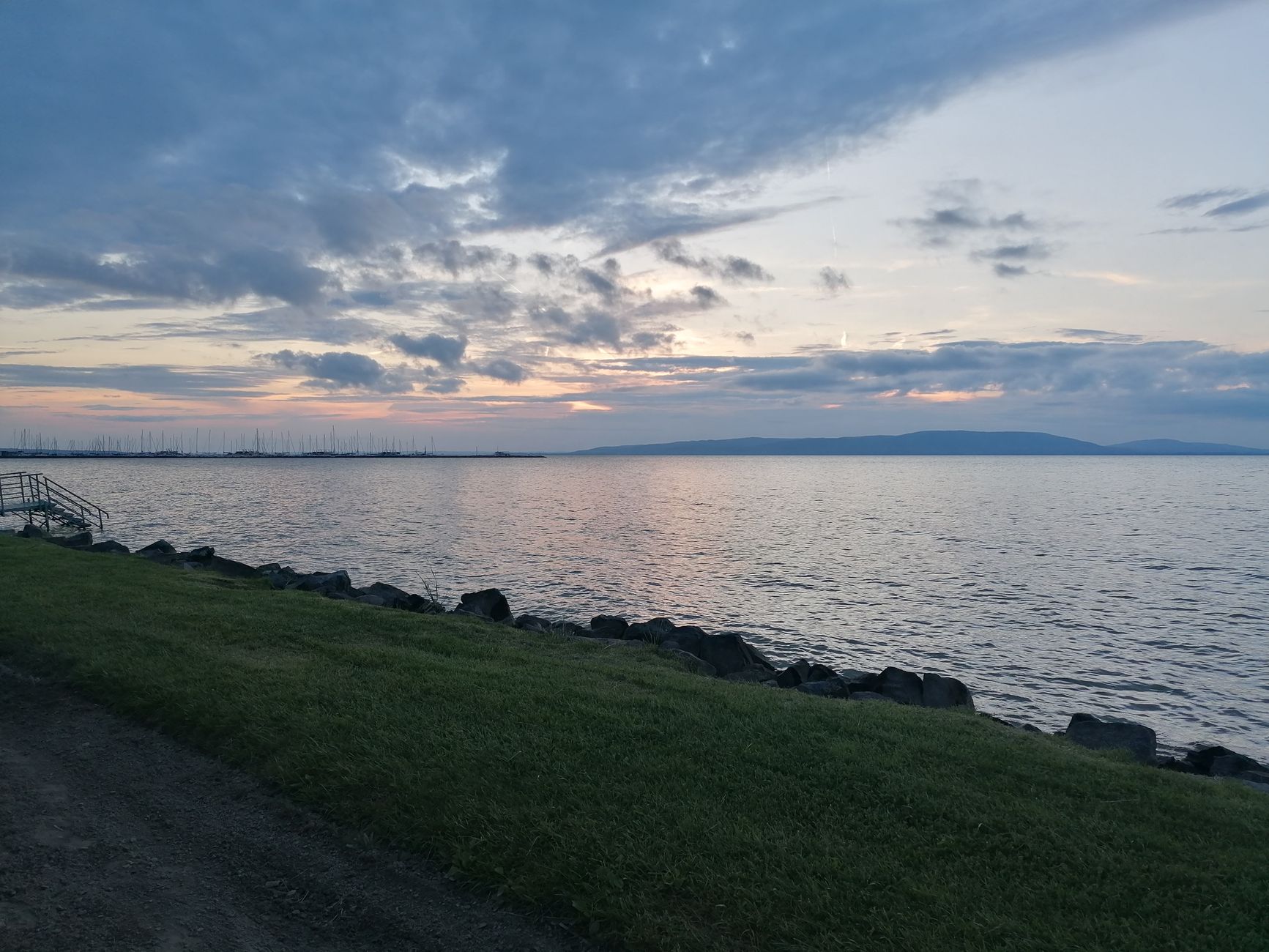 Serene view of Lake Balaton at twilight, with calm waters and soft clouds.