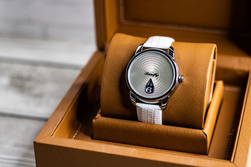 A white-strap watch resting in a tan leather box — photo by Maksim on Pexels