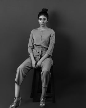 Sepia-toned portrait of a stylish young woman sitting on a stool in minimalist attire.