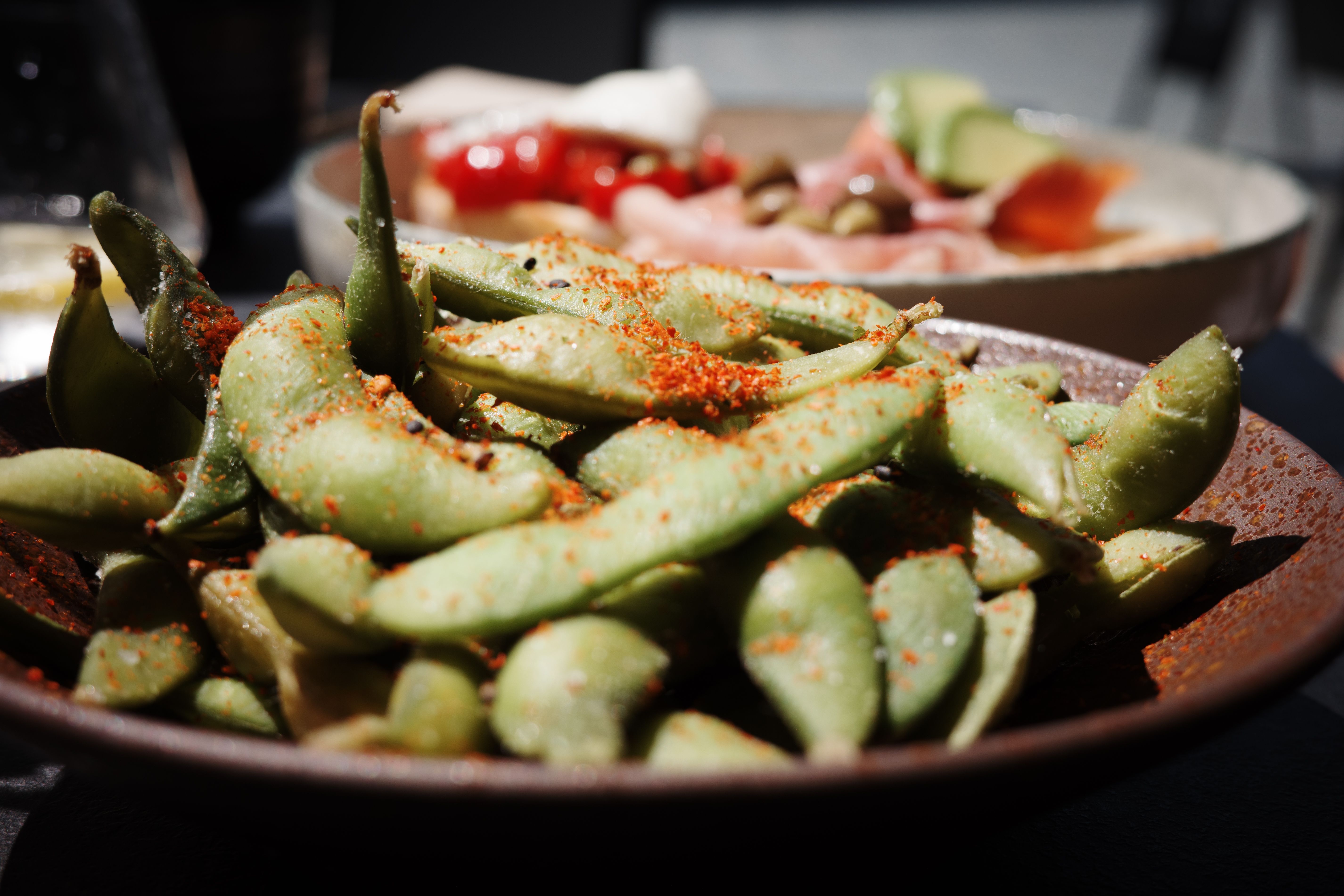 A close-up of spicy edamame served alongside Italian cold cuts, capturing the rich textures and vibrant colors.
