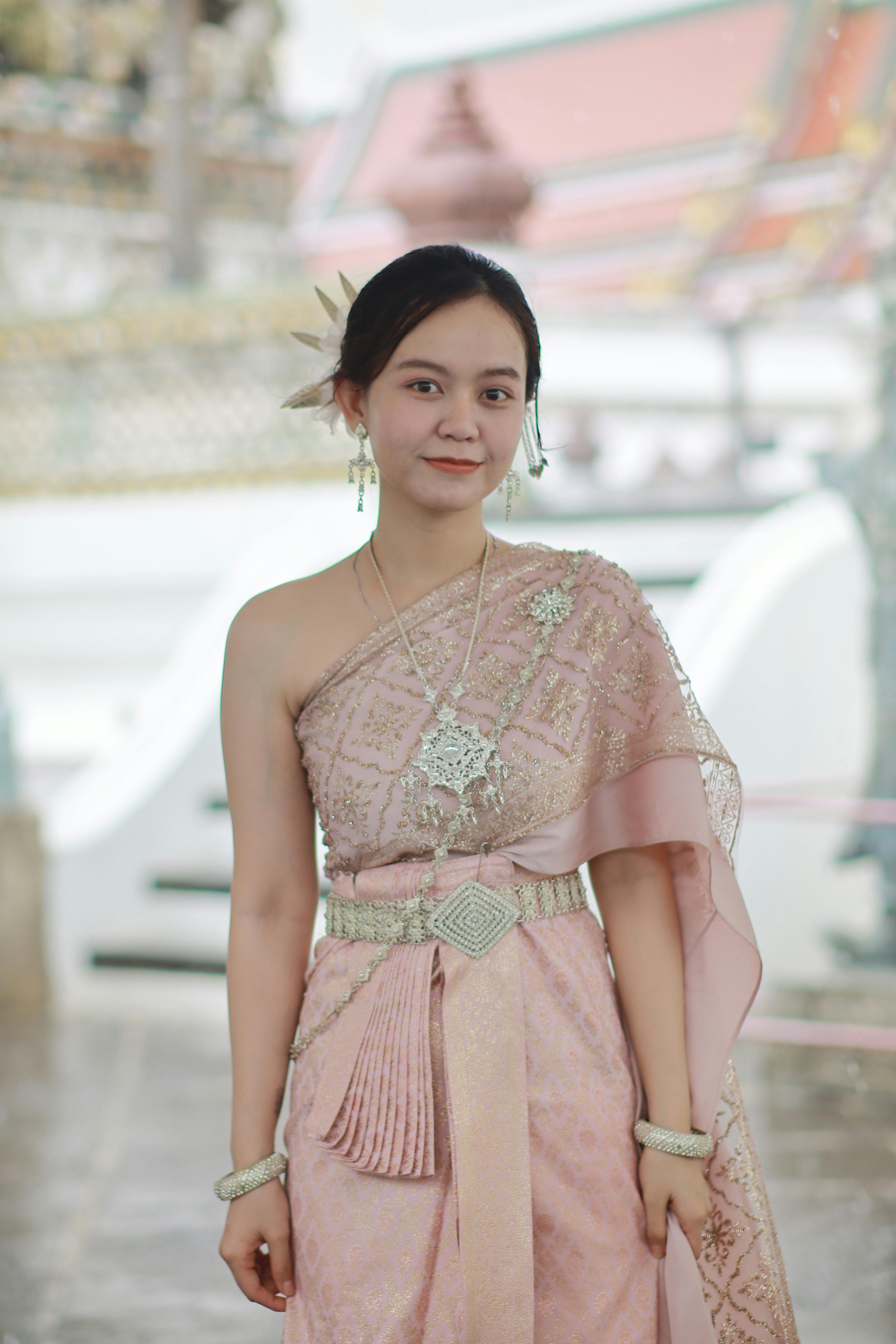 Woman in elegant Thai attire standing indoors at a cultural site.