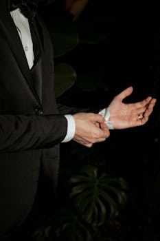A close-up of an elegant man adjusting his suit cuff outdoors at night.