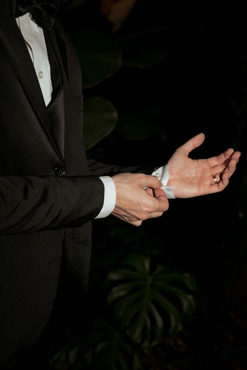 Free A close-up of an elegant man adjusting his suit cuff outdoors at night. Stock Photo