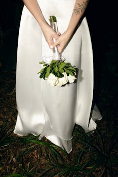 Close-up of a bride holding a white bouquet in a satin dress, outdoors at night.