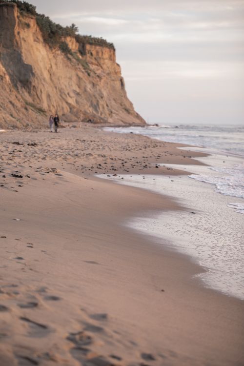 Free A peaceful beach scene at sunrise with towering cliffs and gentle waves. Ideal for nature and travel themes. Stock Photo